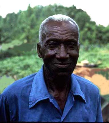 An old man in a blue shirt standing in a field.
