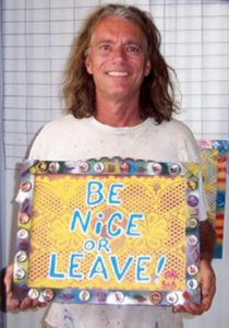 A man holding up a sign that says be nice or leave.